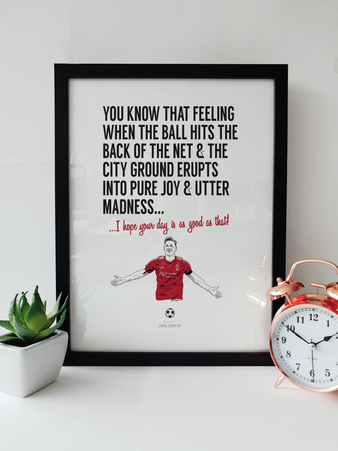 Hand-drawn illustration of Nottingham Forest striker Chris Wood celebrating a goal at the City Ground, created by Local Lingo. The print includes bold text that reads: "You know that feeling when the ball hits the back of the net & the City Ground erupts into pure joy & utter madness... I hope your day is as good as that!" Displayed in a black frame.