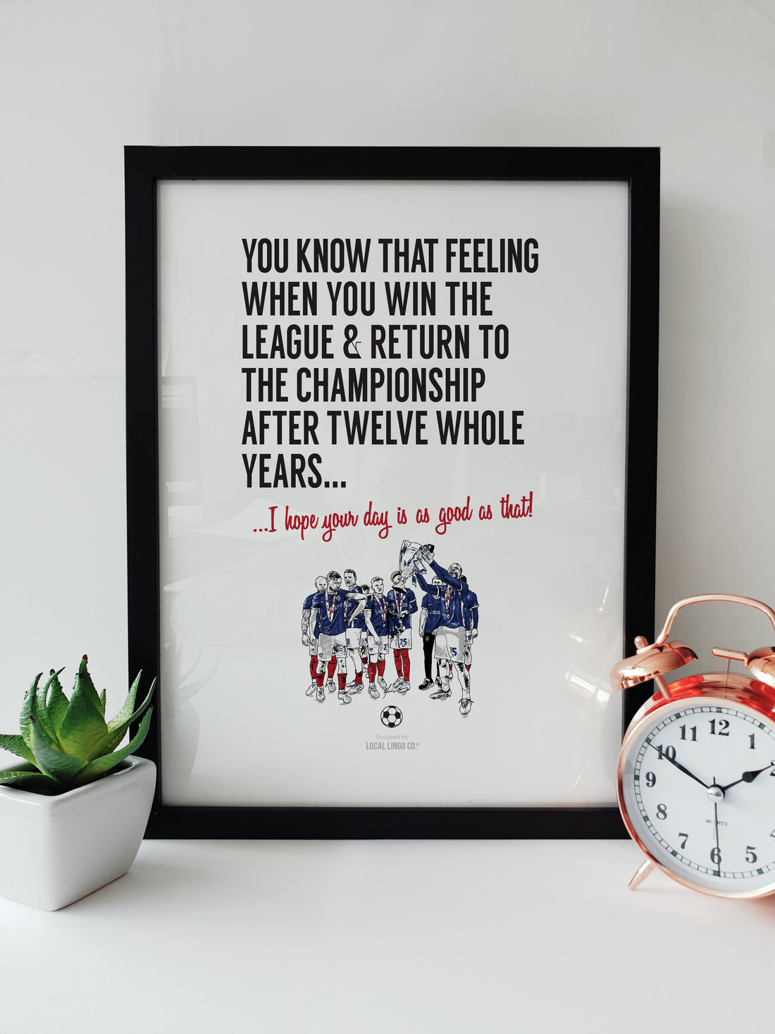 Framed Portsmouth FC Promotion Print featuring a team celebration illustration and inspirational message, displayed on a white desk. designed by local lingo