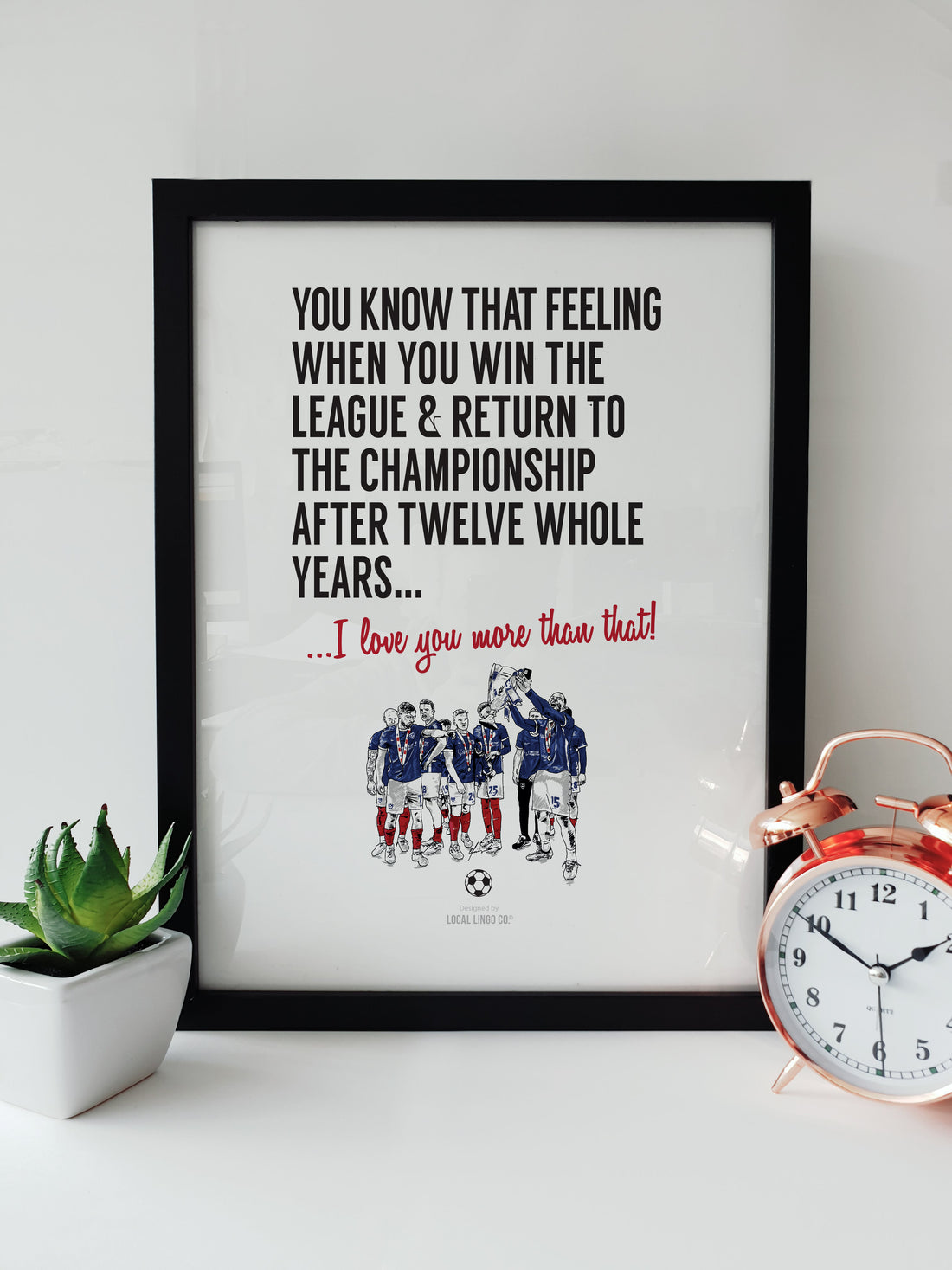 Framed Portsmouth FC Promotion Print featuring a team celebration illustration and inspirational message, displayed on a white desk. 2024 championship keepsake designed by local lingo