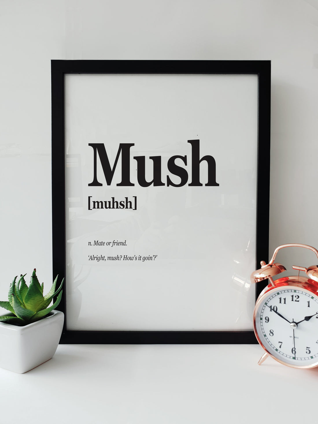 Framed Portsmouth Dialect Print featuring the word "Mush" with pronunciation and definition, displayed on a white desk with a plant and a copper alarm clock. Pompey translation designed by local lingo